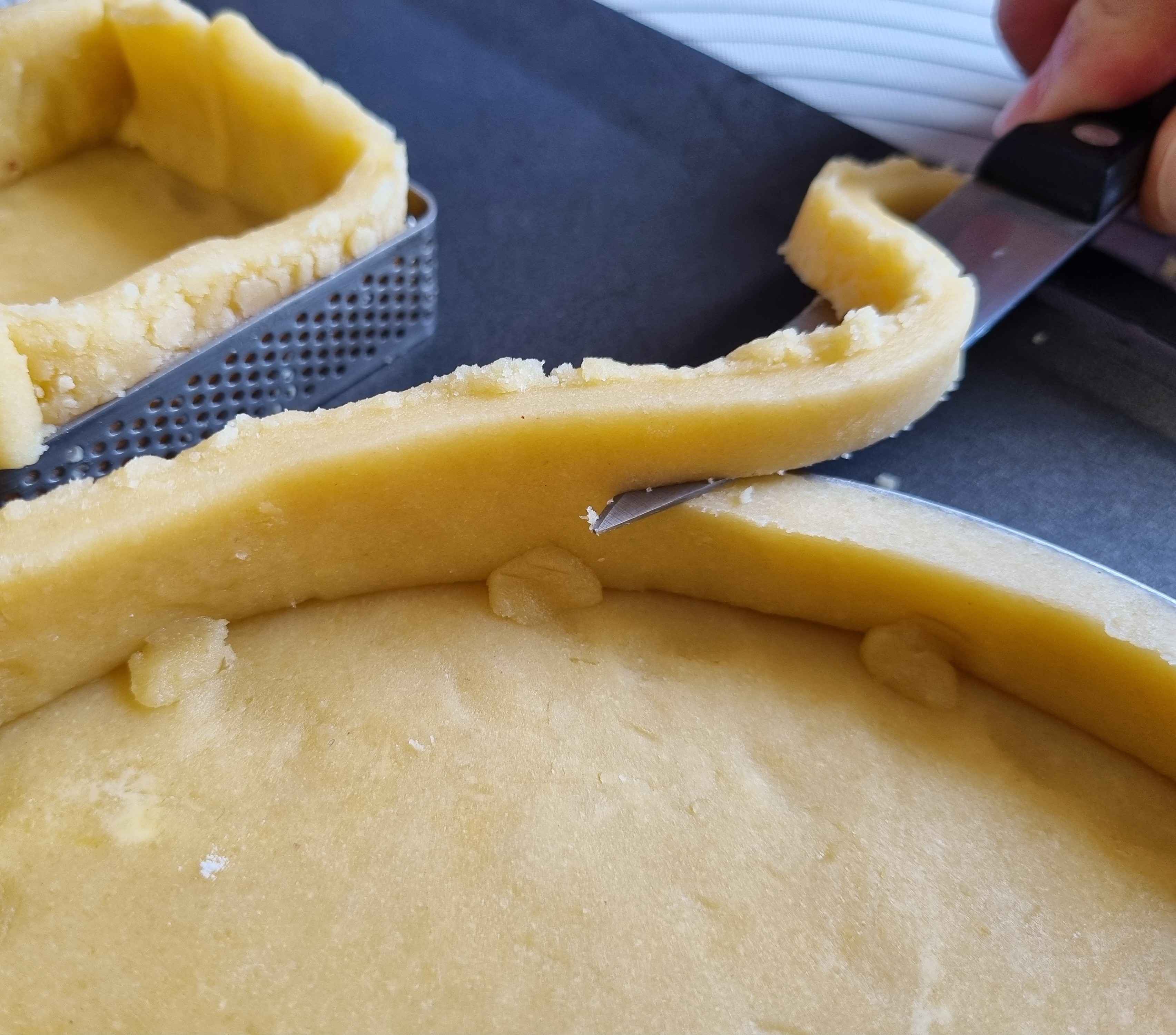Trimming excess dough from the sides of the tart rings.