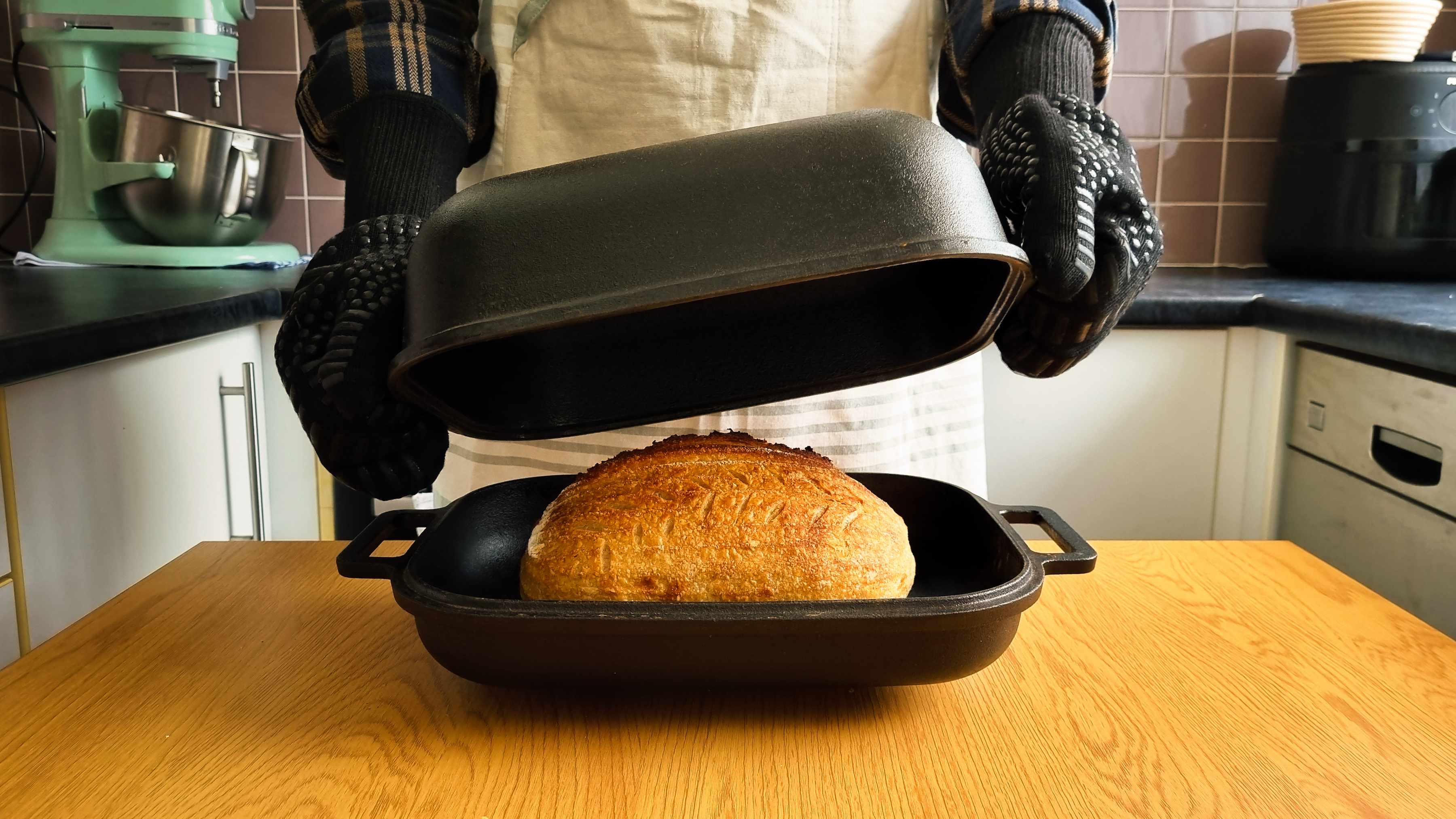 The author lifting the lid of a cast iron pan to reveal a freshly baked loaf of bread.