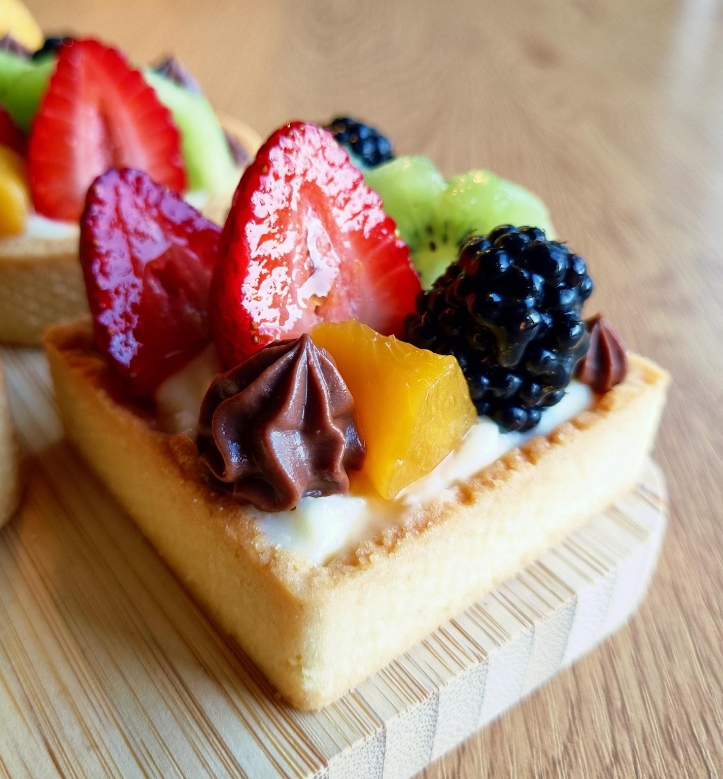 A close-up of a single fruit tartelette on a wooden board, showing the shiny glaze on the fresh fruit.