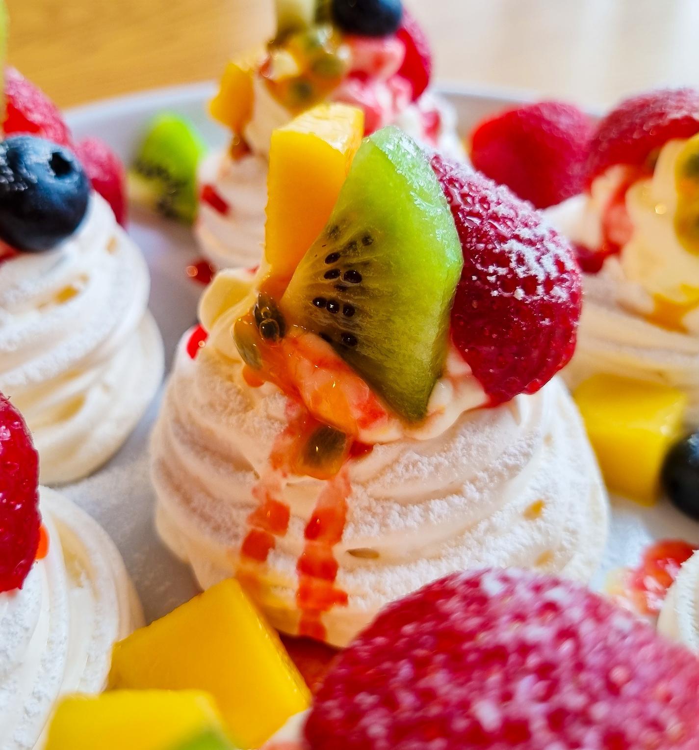 Mini pavlovas on a plate garnished with fruit and icing sugar.