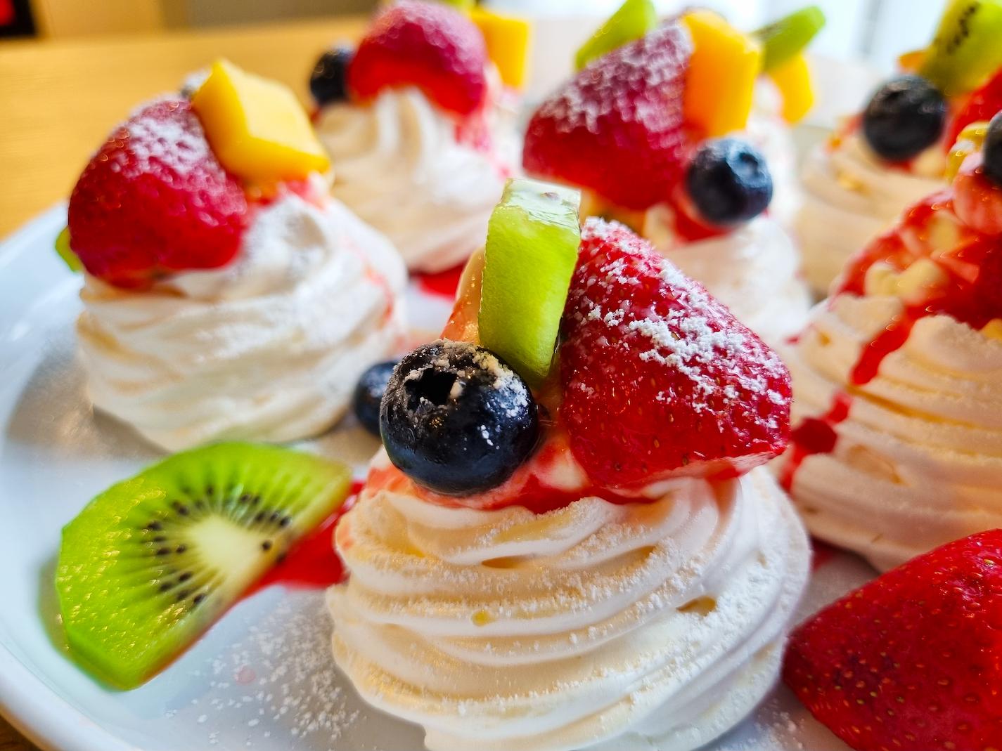 Mini pavlovas on a plate garnished with fruit and icing sugar.