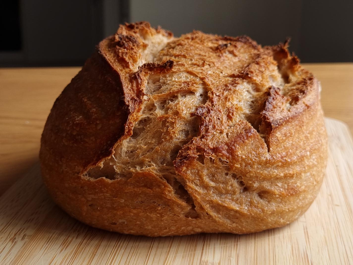 A baked, golden brown spelt sourdough loaf, sitting on a wooden board.